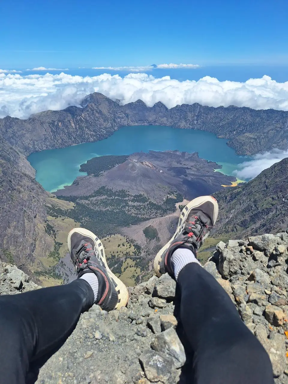 Trekker resting on the Mount Rinjani summit, looking down at Segara Anak crater lake